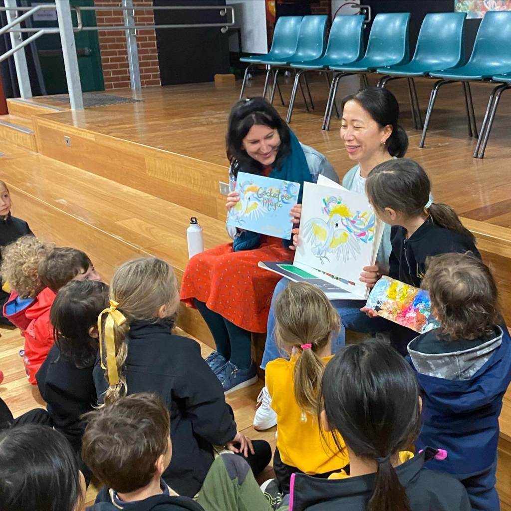 Image of author Katharine Rogers and Illustrator Nana Sakata rading Cockatoo Magic to a group of children sitting on the floor. They are smiling.