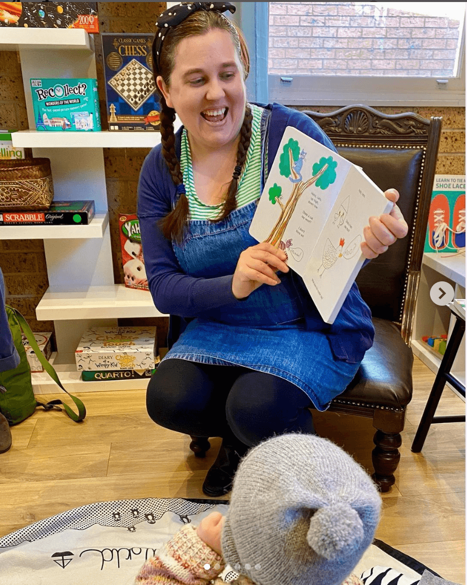 Image of Sharon Baldwin reading a children's book in a shop. We can see a child sitting on the floor